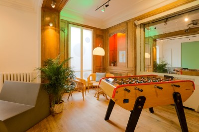 Salon lumineux avec parquet en bois clair, cheminée, fauteuils bleus et moulures au plafond.