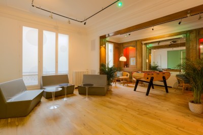 Salon lumineux avec parquet en bois clair, cheminée, fauteuils bleus et moulures au plafond.