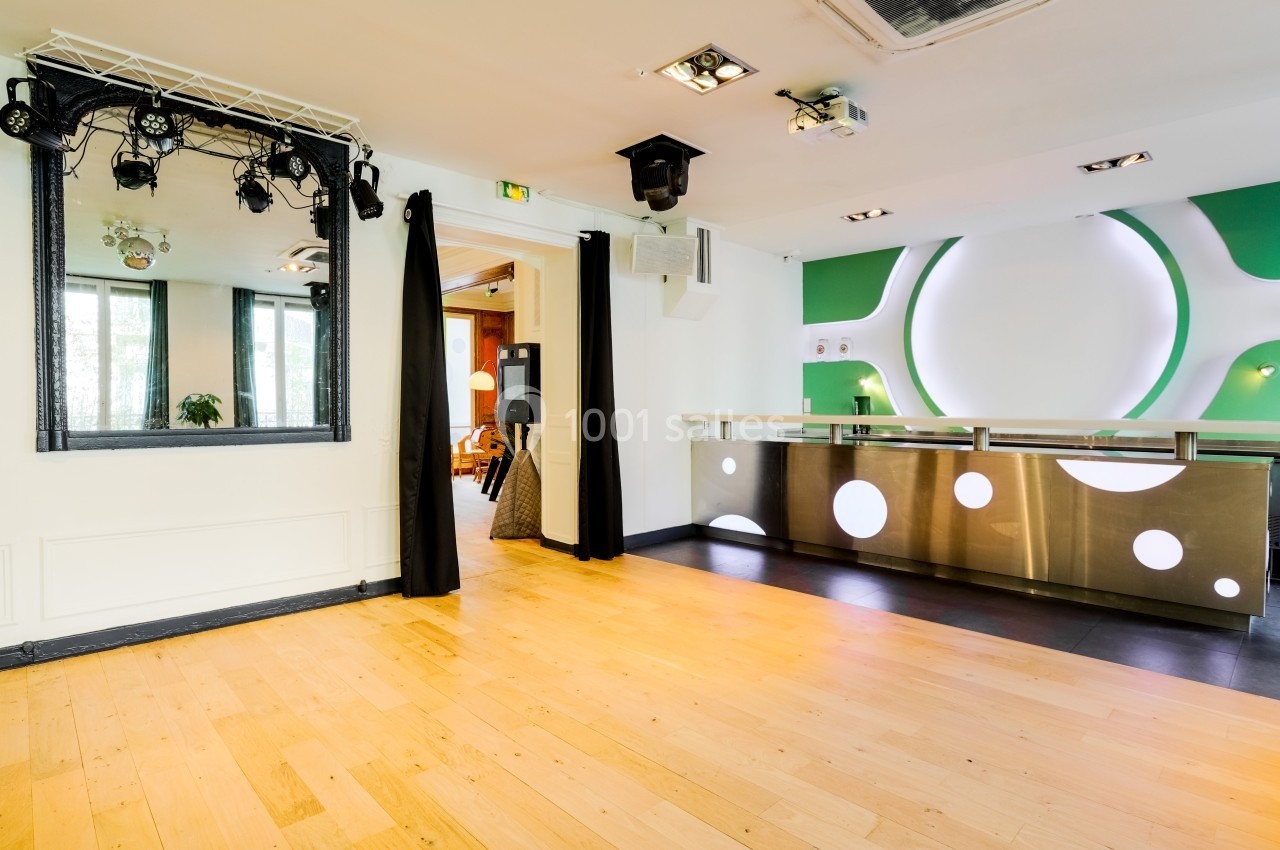 Salle lumineuse avec parquet, comptoir moderne en métal, miroir encadré noir et éclairages suspendus.