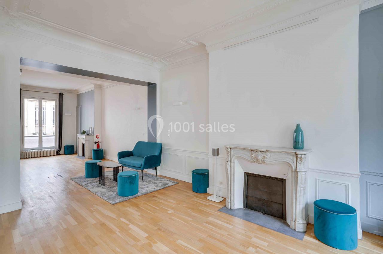Salon lumineux avec parquet, cheminée décorative blanche, mobilier bleu et grande ouverture vers une autre pièce.