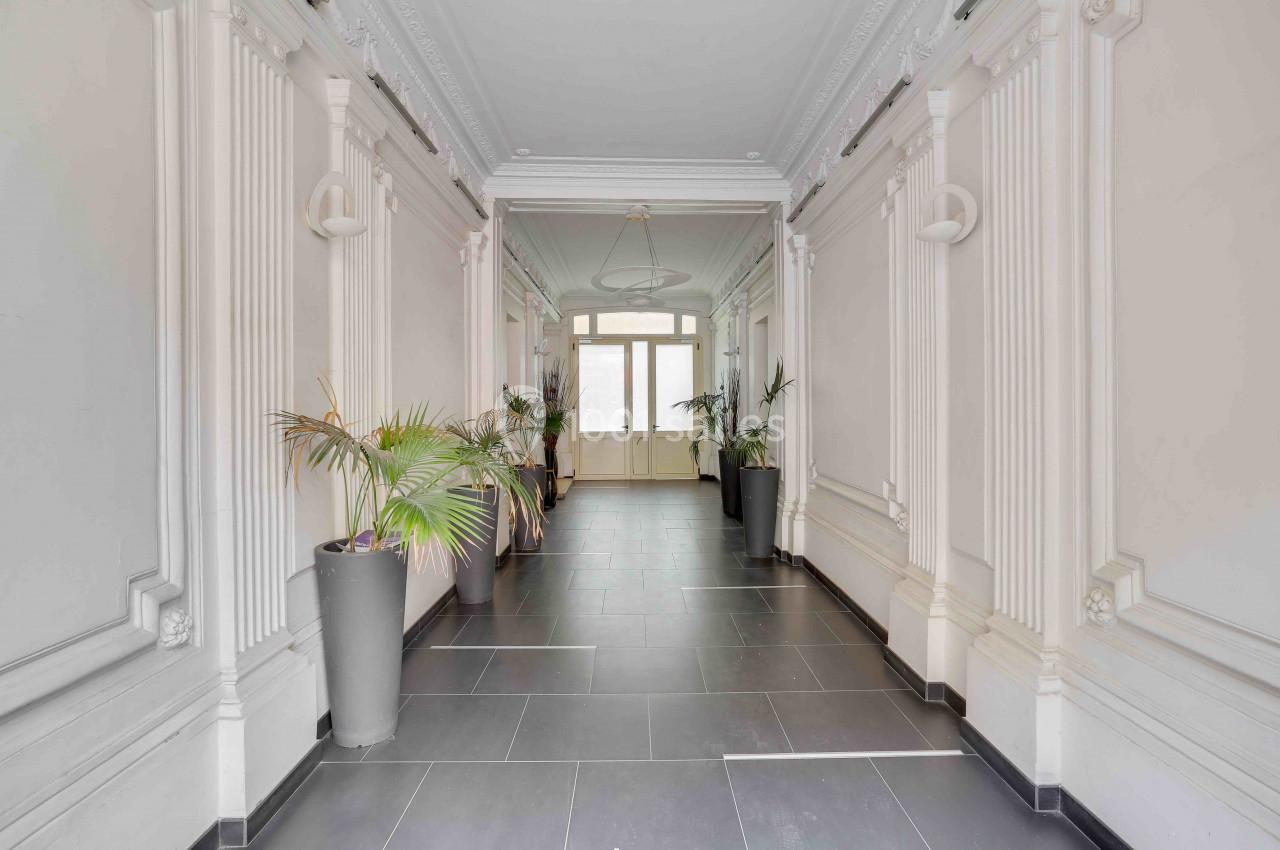 Couloir lumineux avec carrelage sombre, moulures décoratives blanches et plantes en pots près des murs.