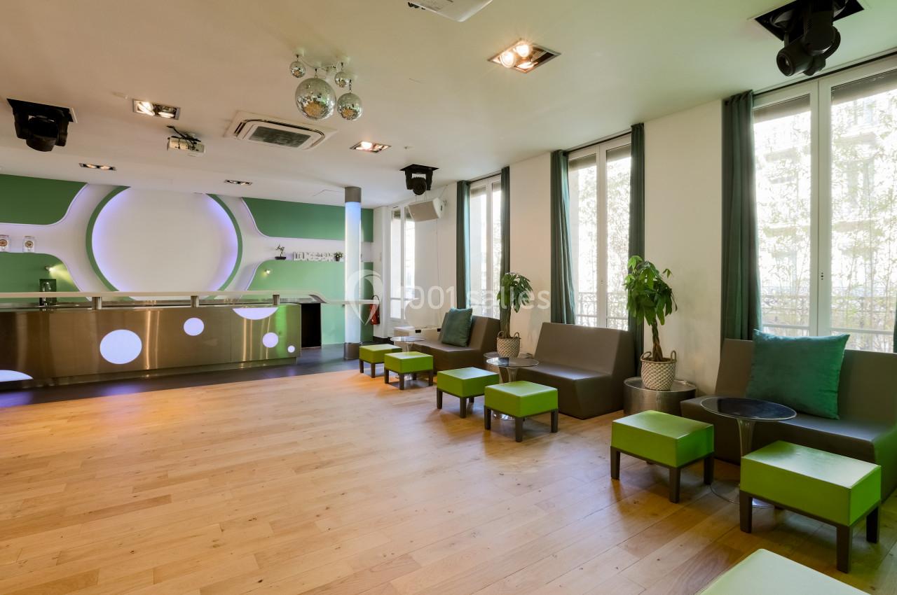 Salle lumineuse avec parquet en bois clair, mobilier vert et marron, et comptoir moderne dans un décor vert et blanc.