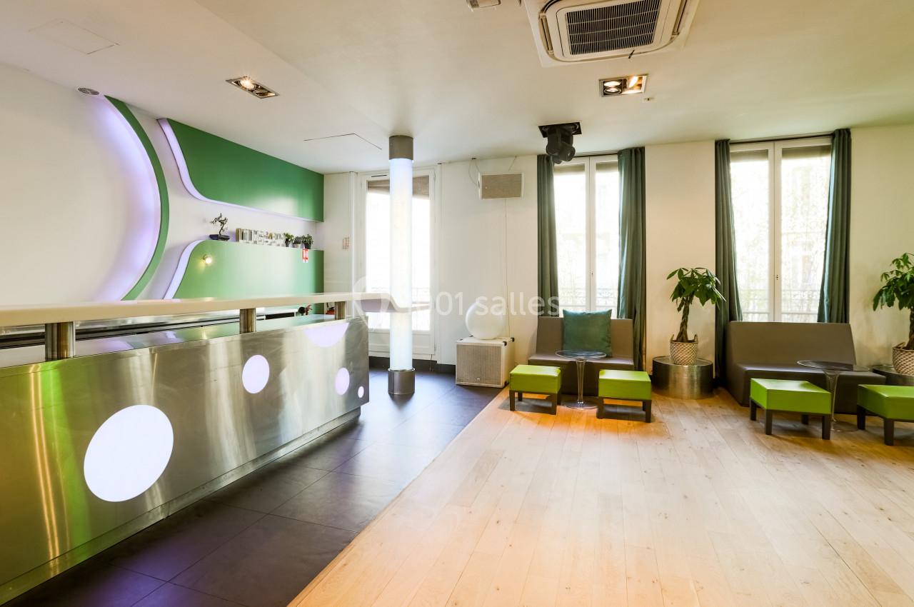 Intérieur lumineux avec comptoir moderne, sièges verts, plantes et grandes fenêtres laissant entrer la lumière naturelle.