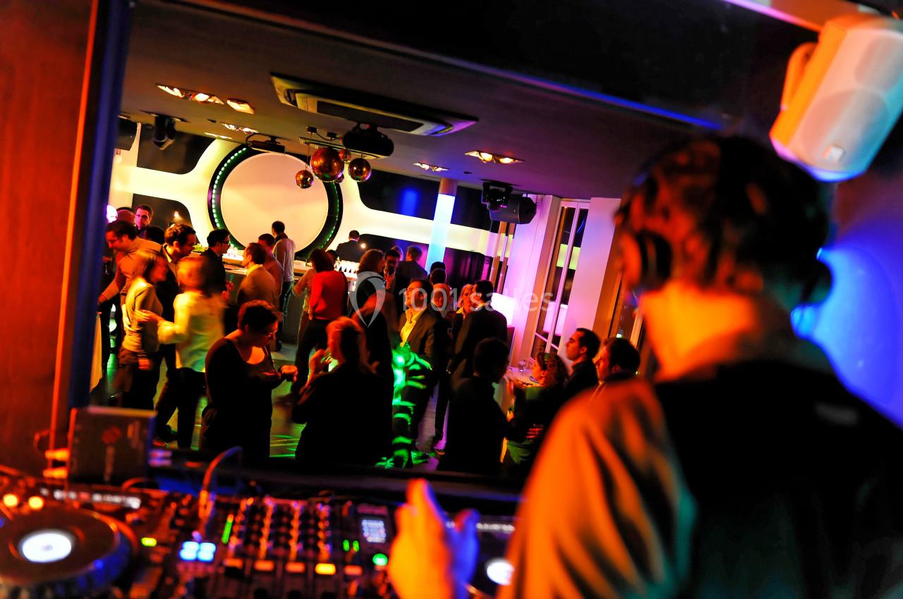 Un DJ mixe devant une foule dansante dans un club éclairé par des lumières colorées.