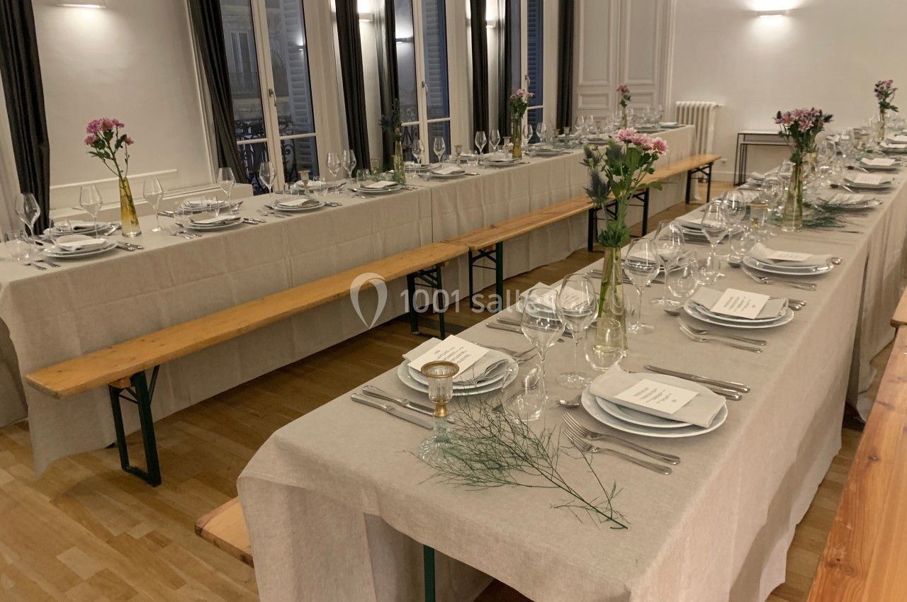 L'Appart Lafayette - diner assis en banquet Tables longues dressées avec nappes beiges, vaisselle élégante, bancs en bois et décorations florales dans une salle…