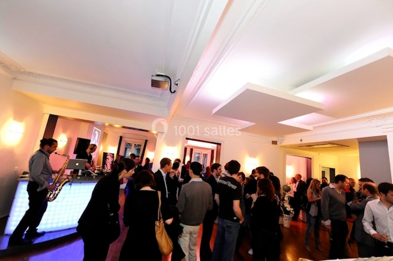 L’Appart Lafayette – parfait pour un cocktail de 100 invités Groupe de personnes discutant dans une salle lumineuse avec un musicien jouant du saxophone près d'un comptoir éclairé.