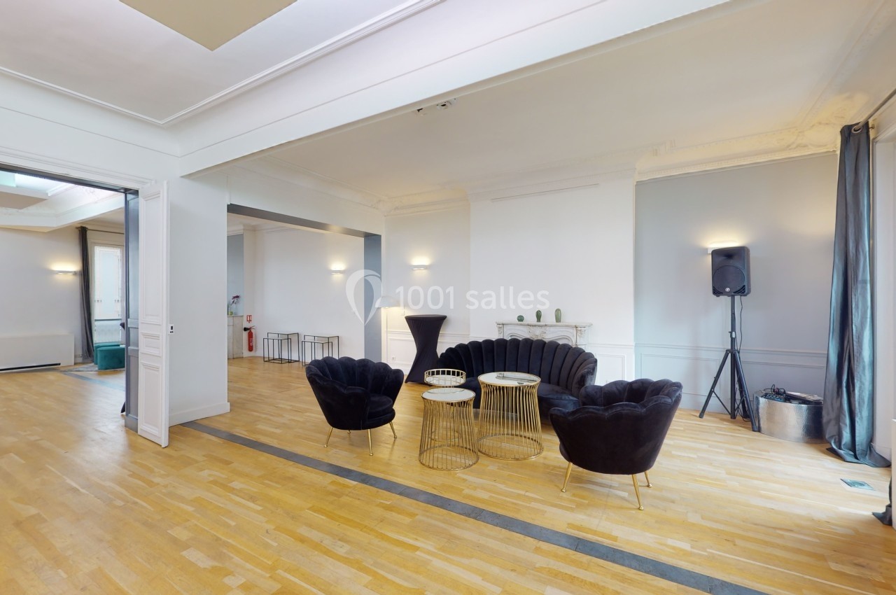 L’Appart Lafayette – un appartement haussmannien modulable pour vos séminaires et réunions Salon lumineux avec parquet, fauteuils noirs, tables basses dorées et grandes fenêtres laissant entrer la lumière naturelle.