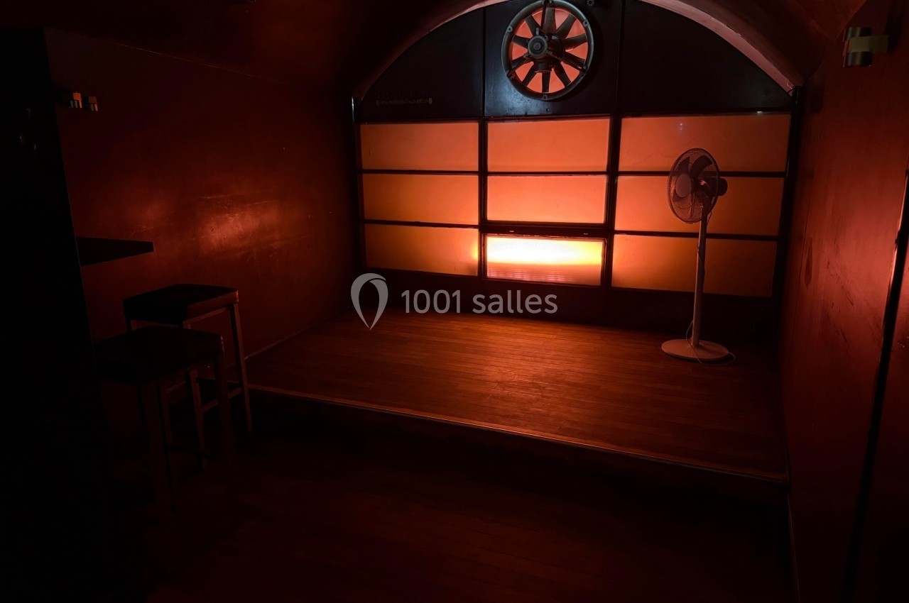 Salle sombre avec un éclairage rouge tamisé, un ventilateur sur pied et un mur avec une fenêtre en demi-cercle.