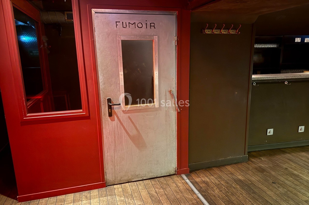 Porte métallique avec fenêtre et inscription ’Fumoir’, située dans un intérieur aux murs rouges et sol en bois.