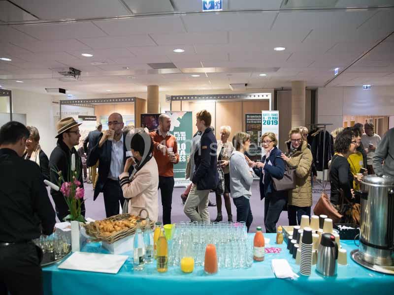 Des personnes discutent et se servent à un buffet avec boissons et collations dans un espace intérieur lumineux.