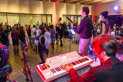 Un groupe de musiciens joue sur scène pendant qu'un public danse dans une salle éclairée et animée.