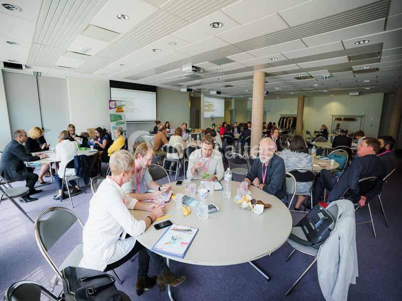 Des personnes discutent en petits groupes autour de tables rondes dans une salle de réunion lumineuse.