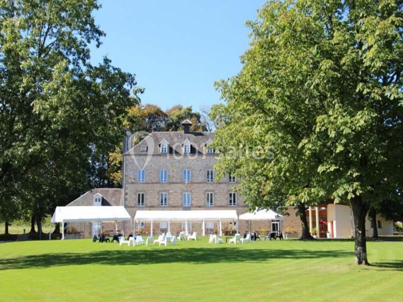 Façade d'un grand bâtiment en pierre entouré d'arbres, avec des chaises et une tente blanche sur une pelouse.