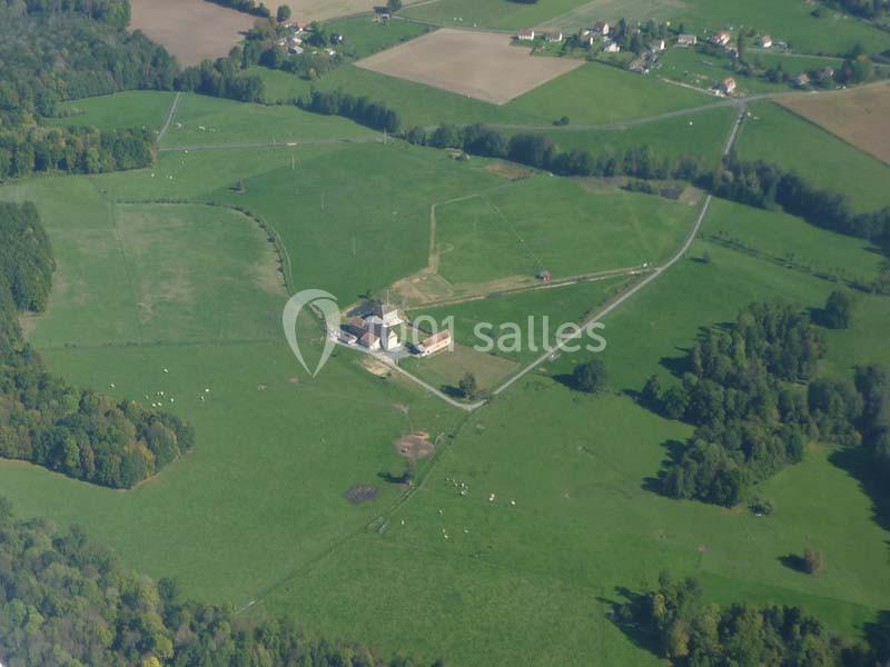Vue aérienne d'une ferme entourée de champs verdoyants, de prairies et d'arbres dans une campagne rurale.