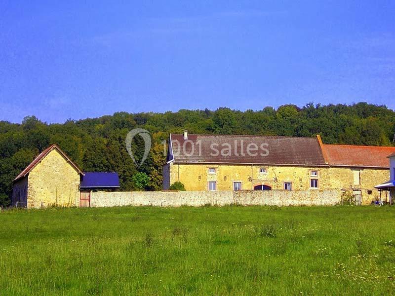Ferme en pierre entourée d'un mur, située dans une prairie verdoyante avec une forêt en arrière-plan.