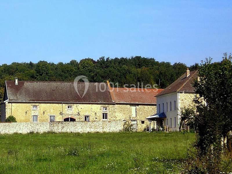 Bâtiments en pierre avec toits en tuiles entourés de verdure, bordés par un mur en pierre, sous un ciel dégagé.