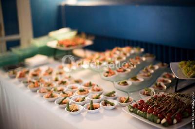 Jardin avec pelouse, tables et chaises rouges, scène en bois, entouré d'arbres et d'une maison à colombages.