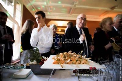 Jardin avec pelouse, tables et chaises rouges, scène en bois, entouré d'arbres et d'une maison à colombages.