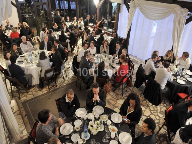 Des convives assis autour de tables rondes lors d'un dîner dans une salle élégante avec rideaux blancs.