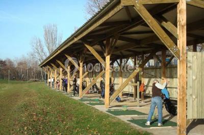 Jardin avec pelouse, tables et chaises rouges, scène en bois, entouré d'arbres et d'une maison à colombages.