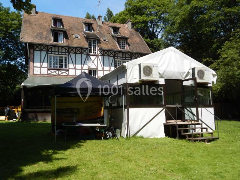 Maison à colombages entourée de verdure avec une structure blanche temporaire et des équipements installés devant.
