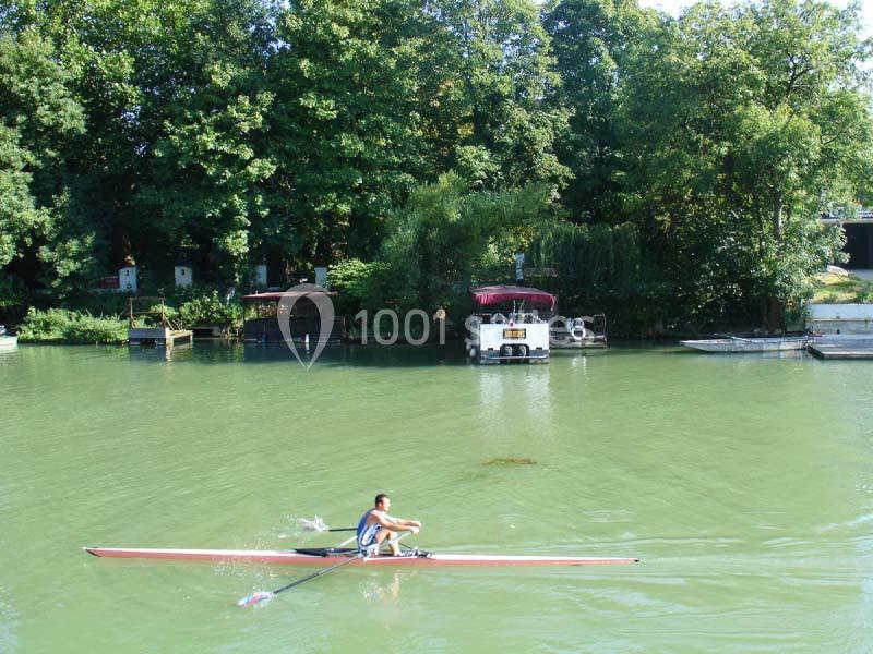 Un rameur seul sur une rivière calme, entourée de végétation et de petites structures au bord de l'eau.