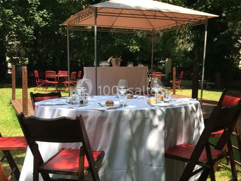 Table dressée avec nappes blanches et chaises en bois, sous un chapiteau dans un jardin verdoyant.