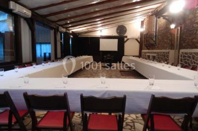 Jardin avec pelouse, tables et chaises rouges, scène en bois, entouré d'arbres et d'une maison à colombages.