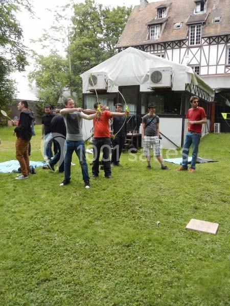 Des personnes pratiquent le tir à l'arc en plein air devant un bâtiment à colombages.