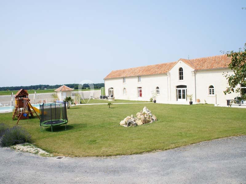 Grande maison en pierre avec jardin, aire de jeux pour enfants, trampoline et piscine, située dans un cadre rural.