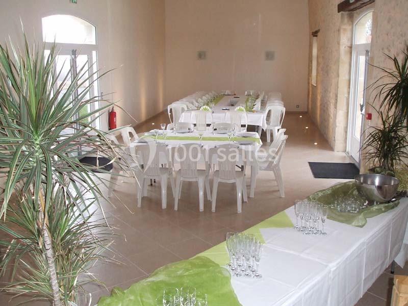 Salle lumineuse aménagée pour un événement avec tables décorées de nappes blanches et vertes, et plantes en décoration.