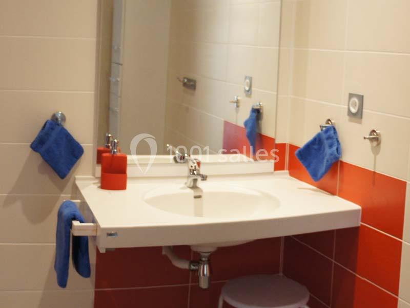 Lavabo accessible avec miroir, serviettes bleues accrochées et carrelage blanc et rouge.