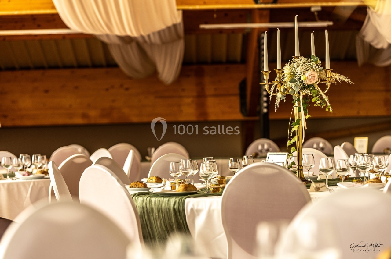 Salle de réception décorée avec des tables rondes, nappes blanches, chandeliers dorés et compositions florales.