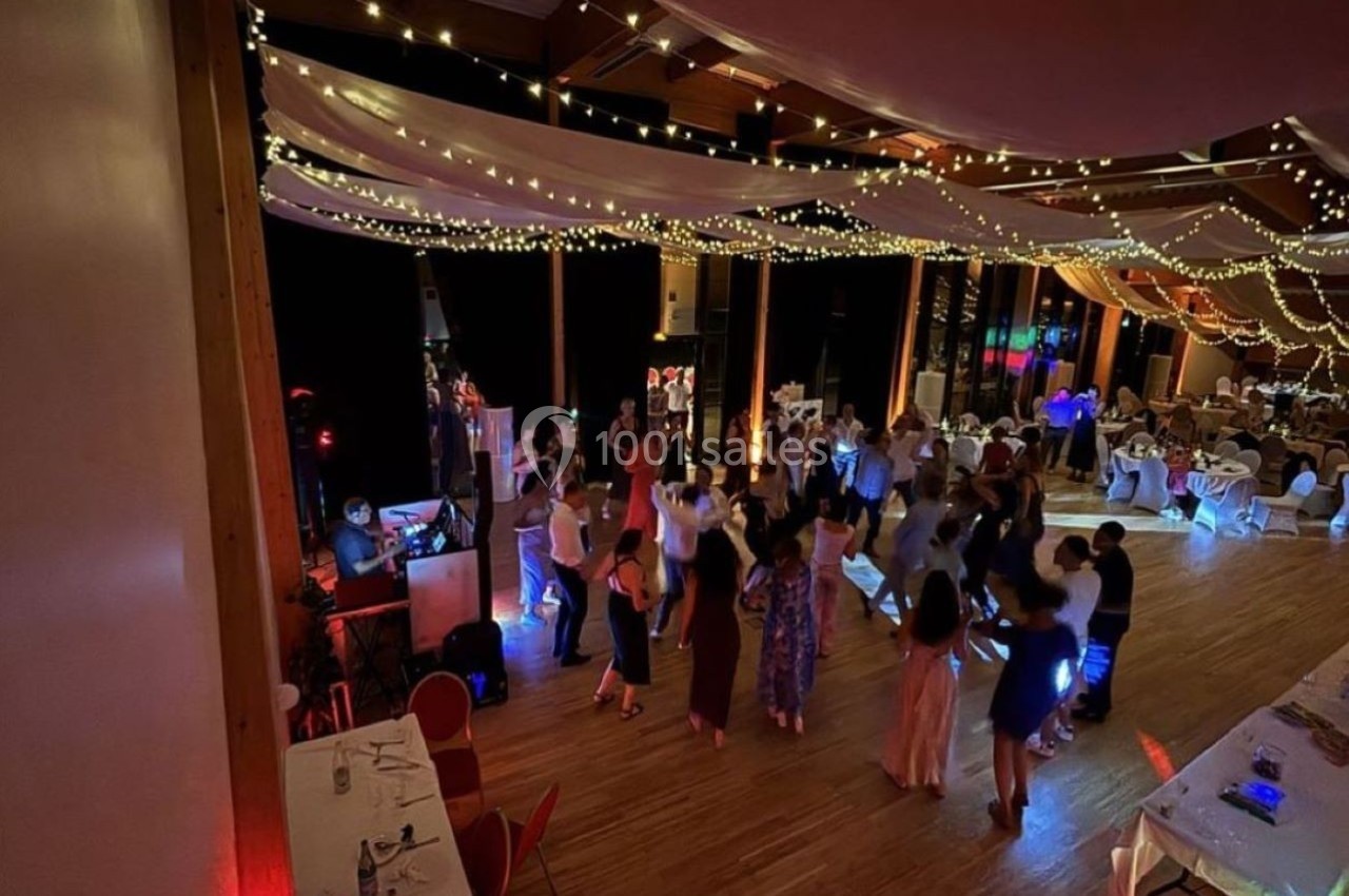 Groupe de personnes dansant dans une salle décorée avec des guirlandes lumineuses et des tables dressées.