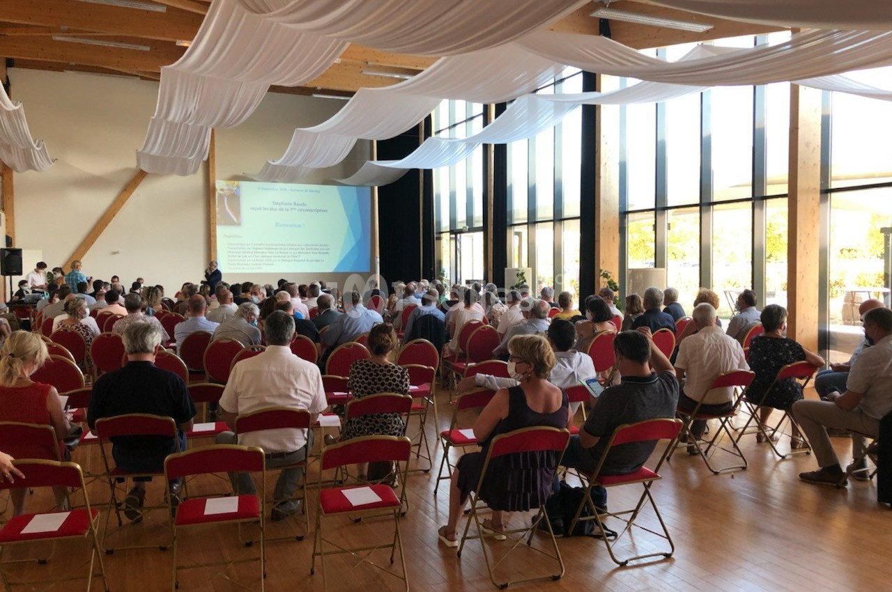 Des personnes assises dans une salle de conférence lumineuse, regardant une présentation projetée sur un écran.