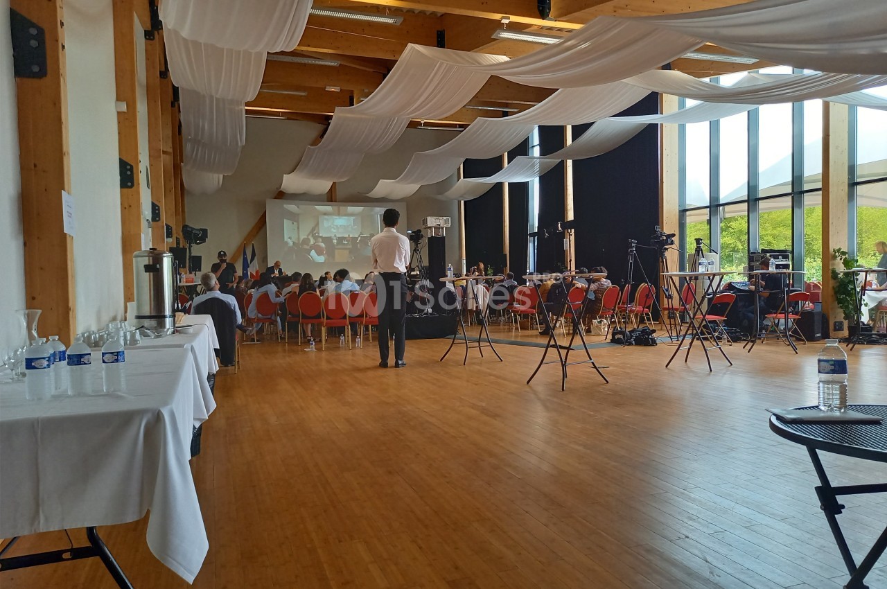 Salle lumineuse avec des participants assis face à un écran de projection, entourés d'équipements audiovisuels.