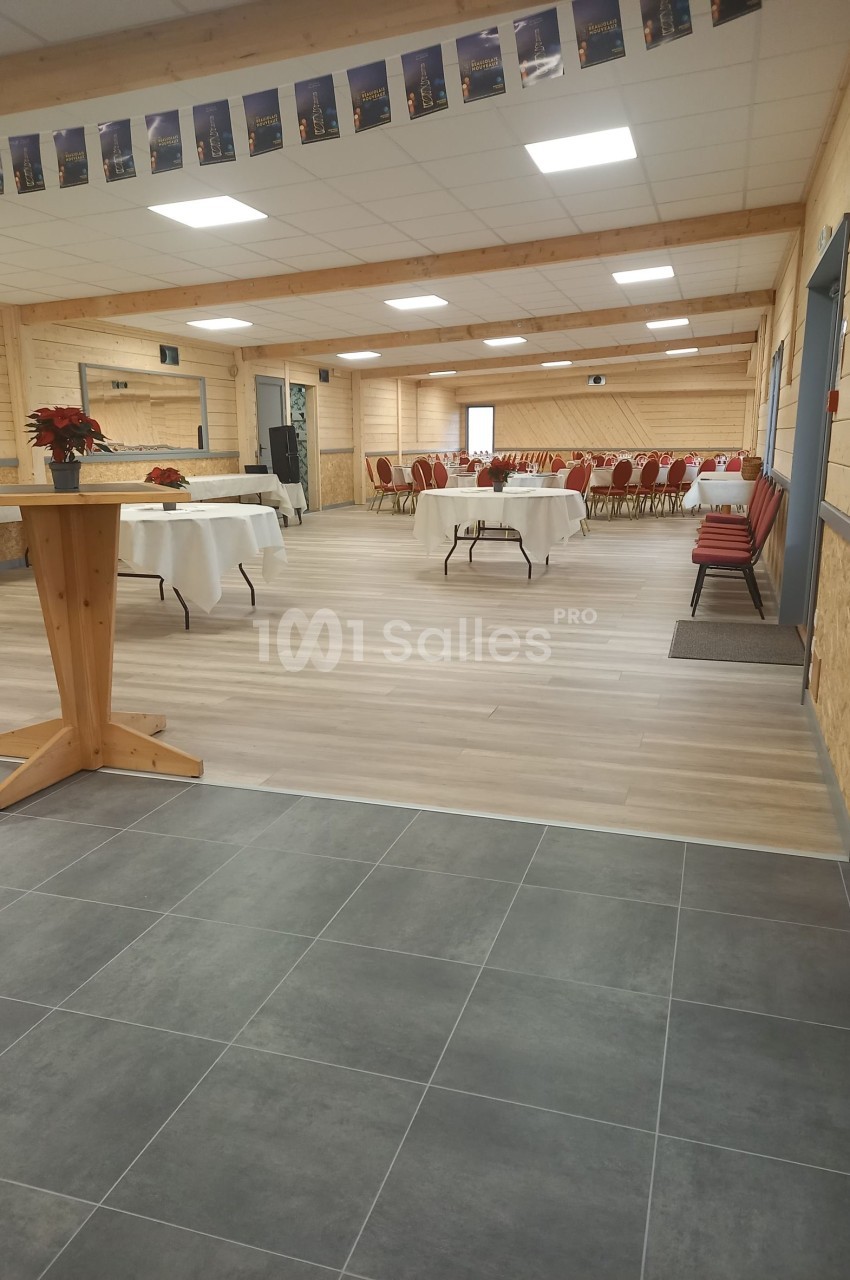 Salle de réception lumineuse avec tables dressées, chaises rouges et décoration sobre dans un espace en bois clair.