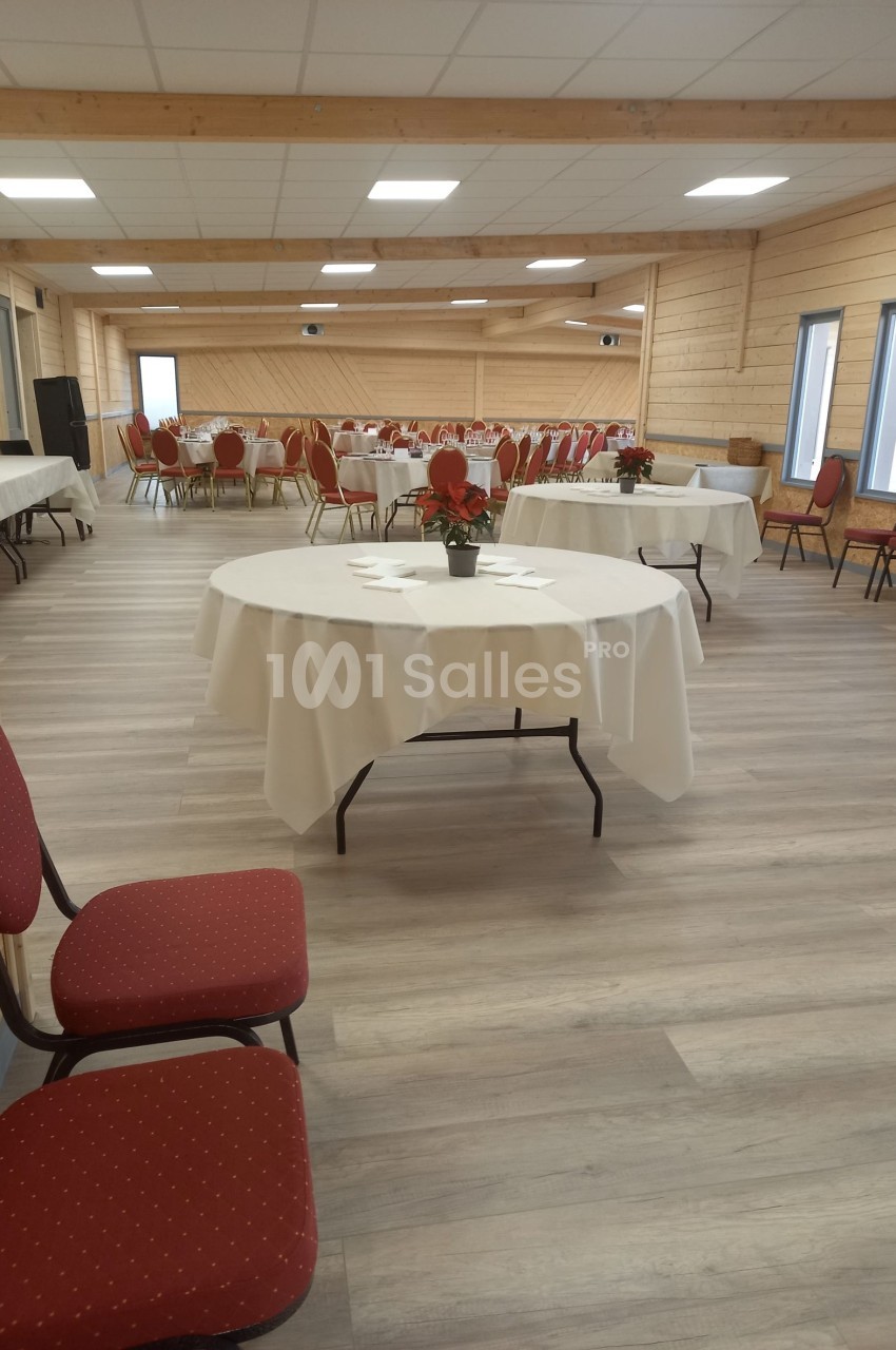 Salle de réception lumineuse avec tables rondes dressées, nappes blanches et chaises rouges.