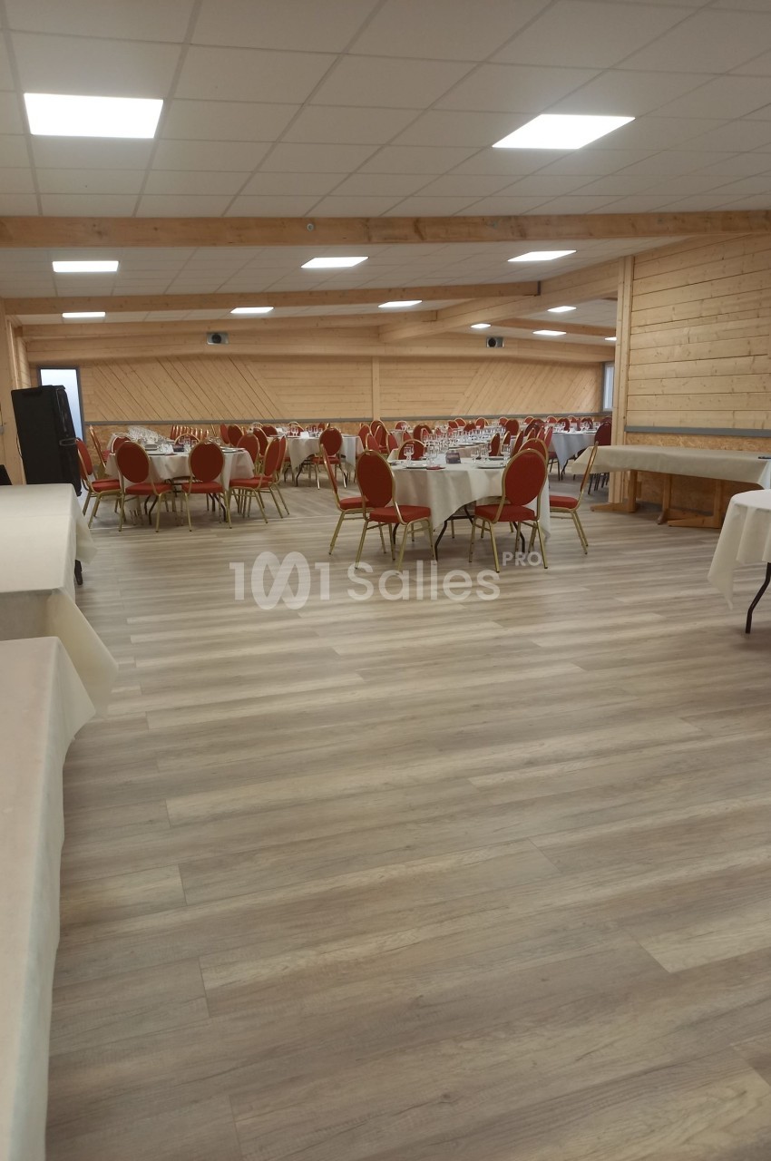Salle de réception avec tables rondes dressées et chaises rouges, éclairée par un plafond à dalles blanches.