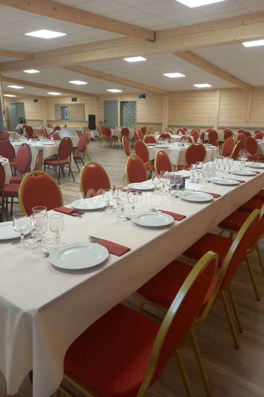 Salle de réception avec des tables dressées, nappes blanches, assiettes, verres et serviettes rouges, prête pour un…