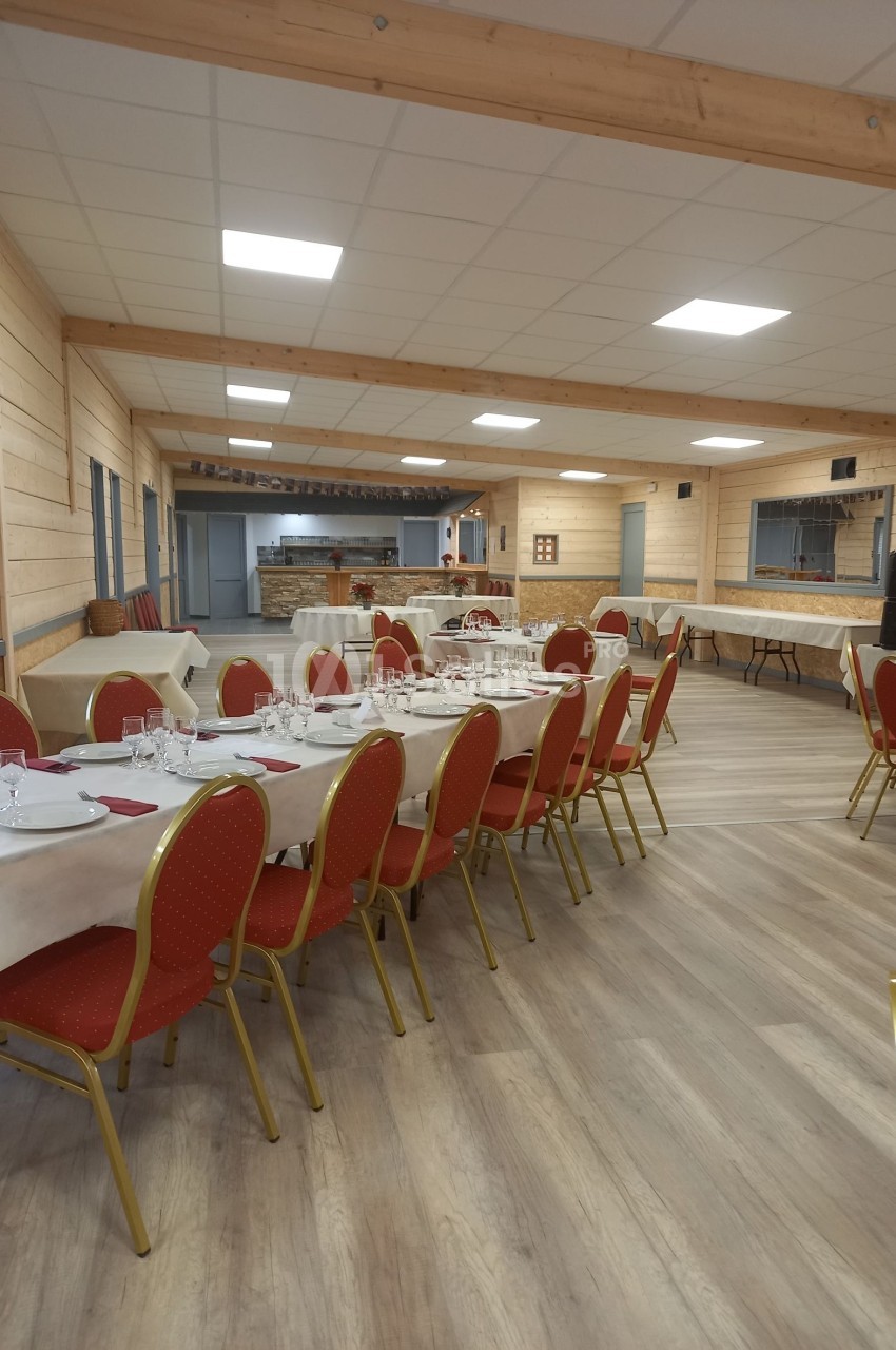 Salle lumineuse avec tables dressées, chaises rouges et parquet clair, prête pour un repas ou un événement.