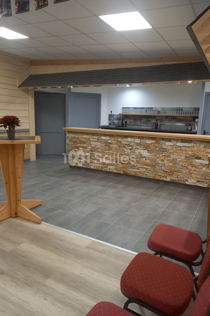 Salle avec comptoir en pierre, tabourets rouges, table haute en bois et éclairage au plafond.