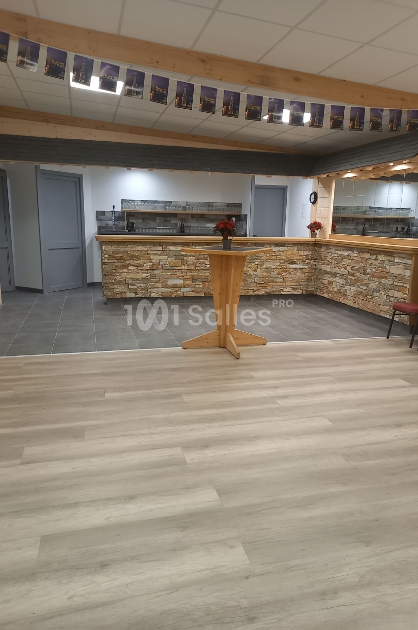 Salle avec un comptoir en pierre, tables hautes en bois, sol en parquet et carrelage, décorée de guirlandes.