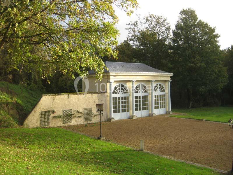 Bâtiment avec grandes fenêtres cintrées entouré de verdure, situé près d'une cour en sable.
