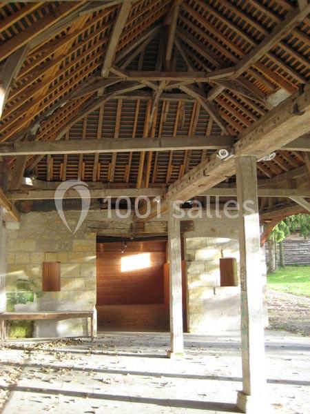 Charpente en bois apparente d'un bâtiment ancien avec murs en pierre et ouvertures lumineuses.