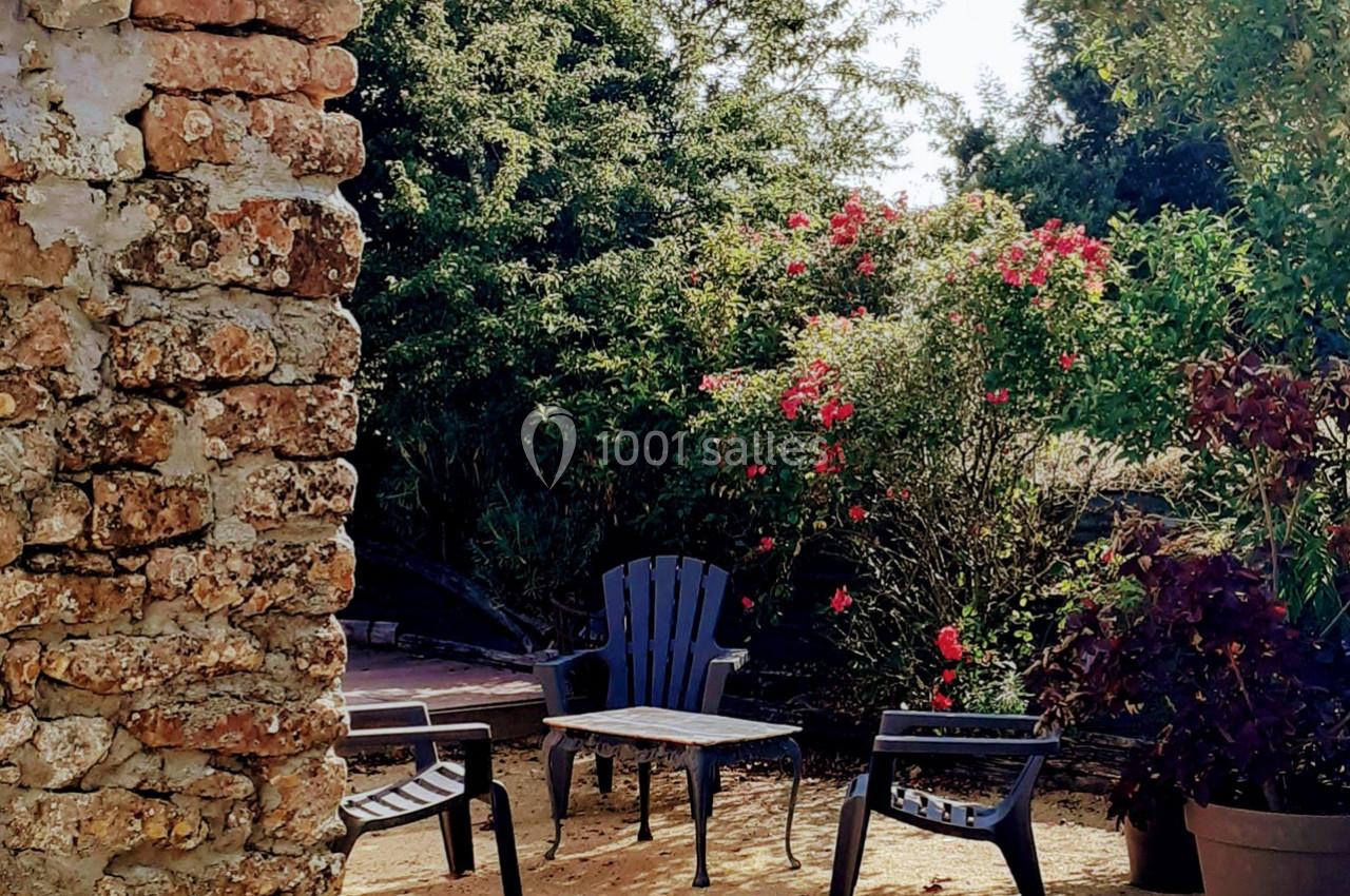 Coin de jardin avec trois chaises en plastique noir autour d'une table basse, entouré de rosiers et d'un mur en pierre.