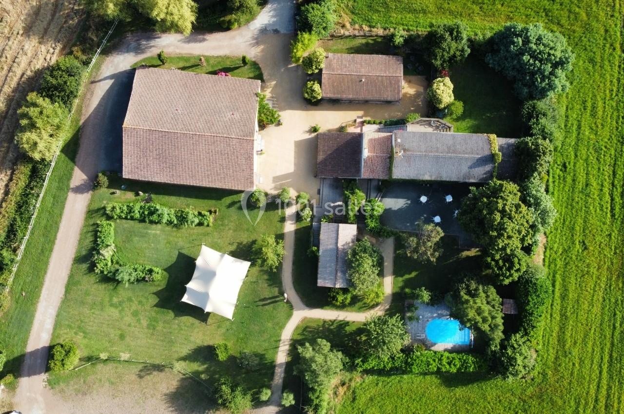 Vue aérienne d'une propriété rurale avec plusieurs bâtiments, un jardin, une piscine et une tente blanche.