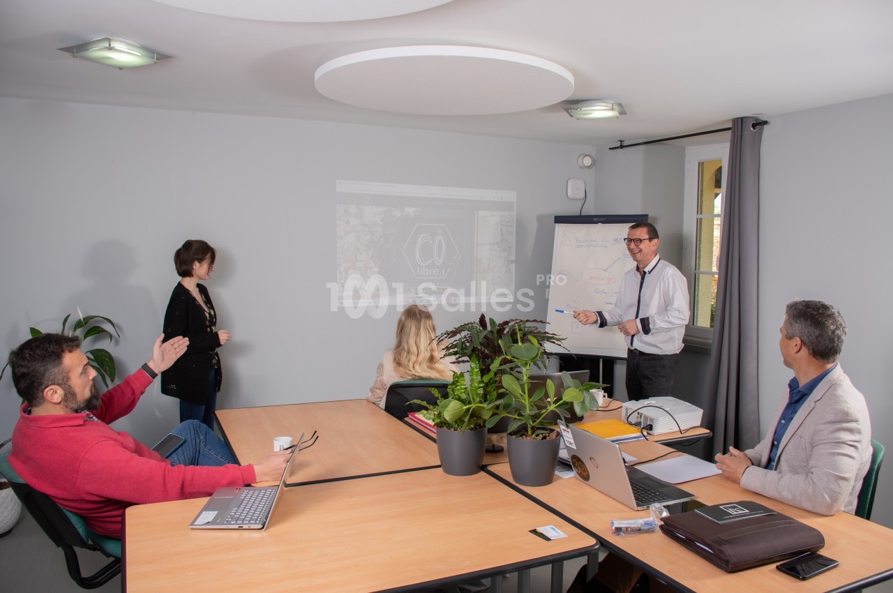 Un groupe de personnes en réunion dans une salle, avec un homme présentant des informations sur un tableau blanc.