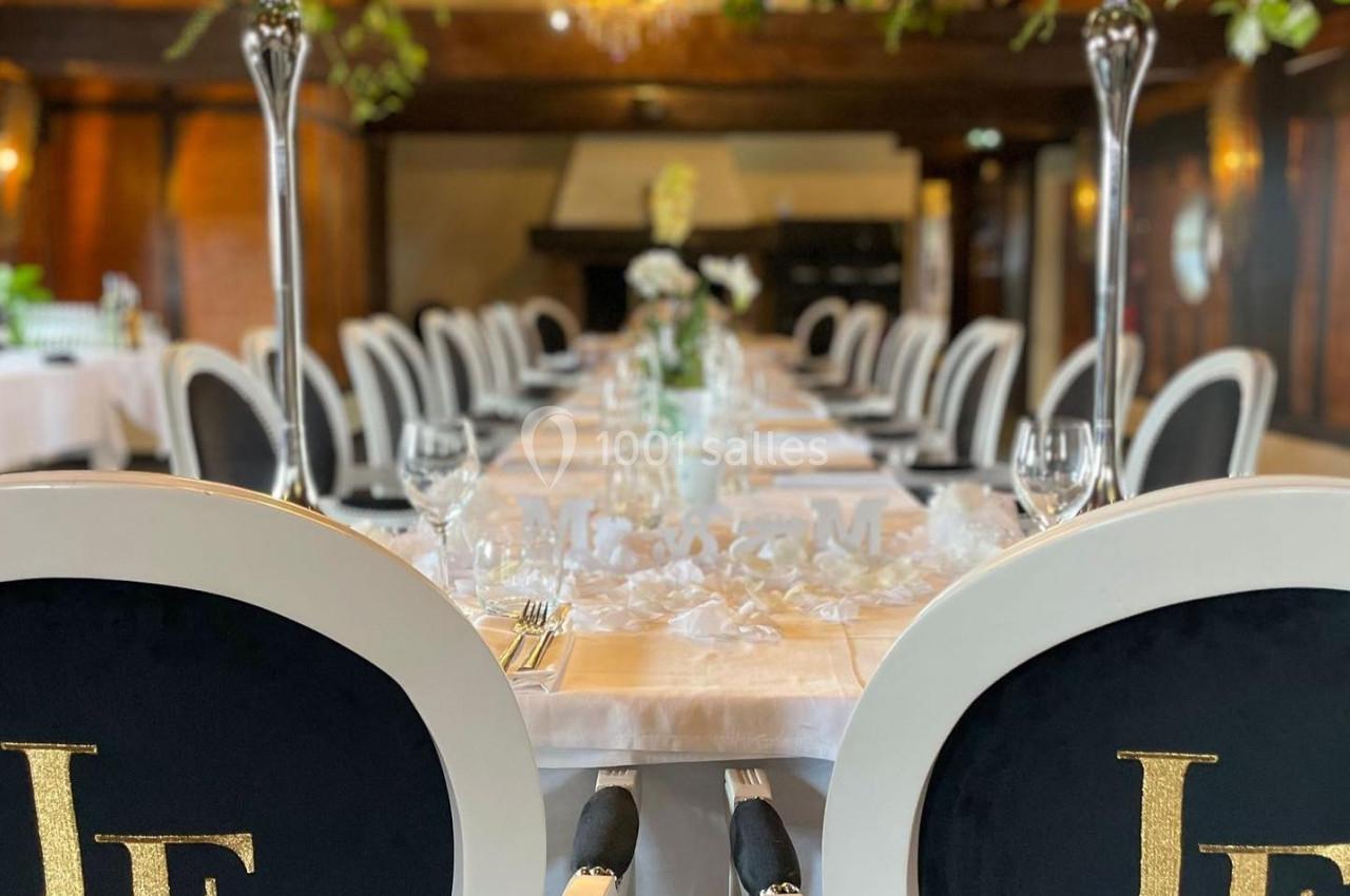 Salle de réception élégante avec tables dressées, chaises noires et blanches, chandeliers et décorations florales.