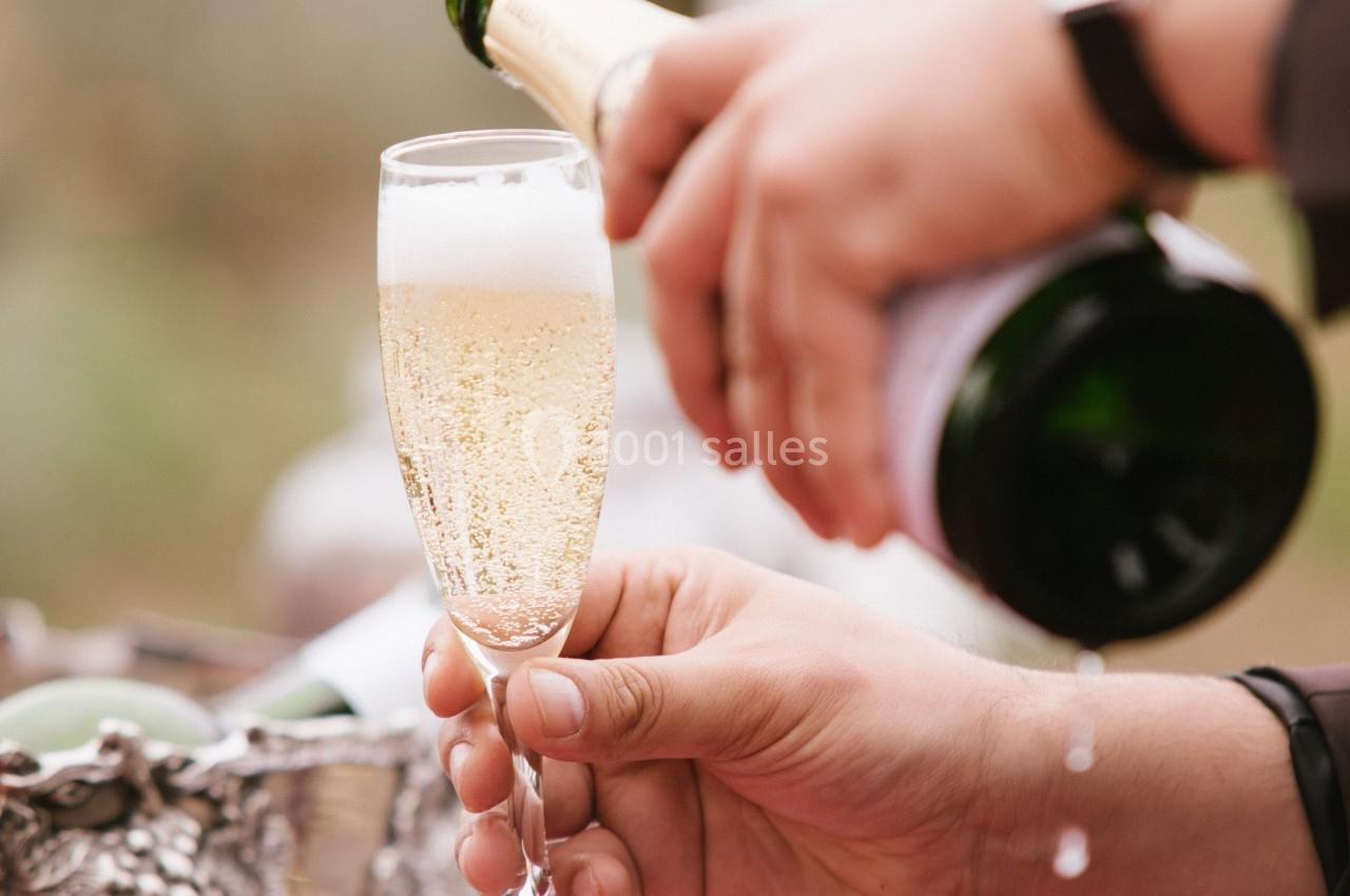 Une main verse du champagne dans une flûte tenue par une autre main, avec un seau à glace en arrière-plan.